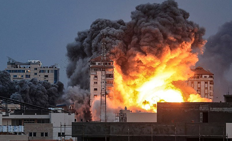 Bombadeiro em edifícios de Gaza em dezembro de 2023. Esta grande explosão é um pequeno fragmento da Nova Bomba Atômica. Imagem da Agência de Notícias Tasnim, licenciada sob CC-BY-SA-4.0 Internacional; via Wikimedia Commons.